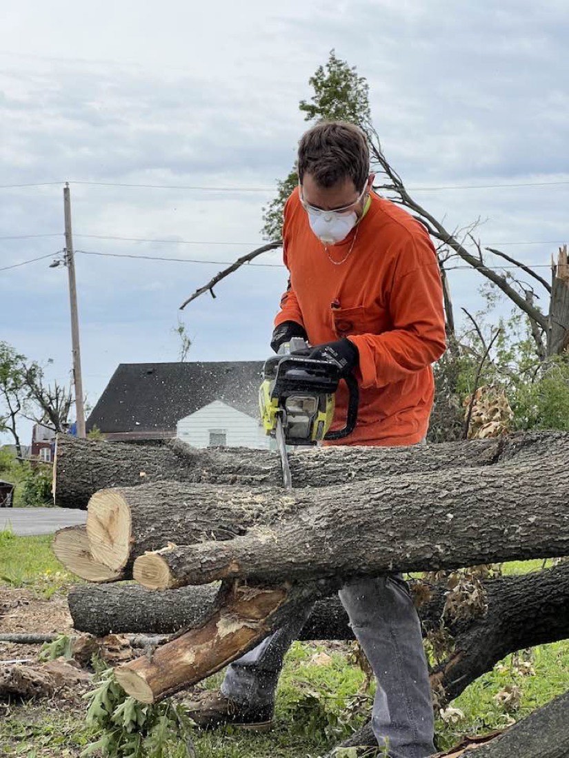A member clearing storm-felled trees with a chainsaw during disaster relief